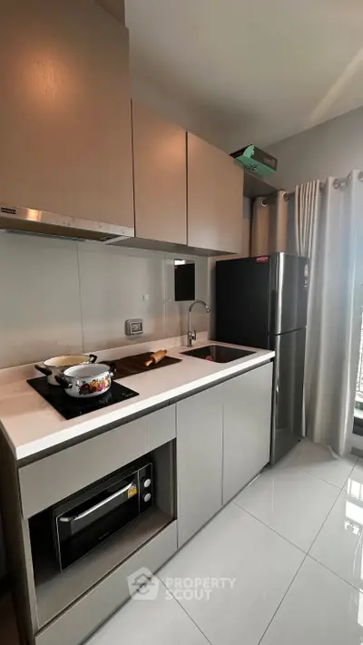 Modern kitchen with sleek cabinetry, gas stove, and stainless steel fridge in a stylish apartment.