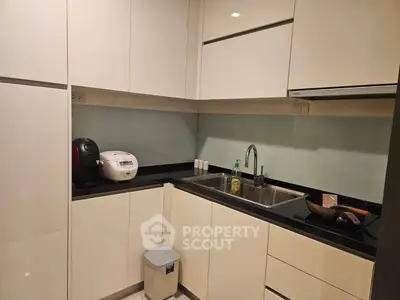Modern kitchen with sleek white cabinets and black countertops, featuring a rice cooker and induction stove.
