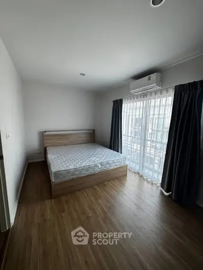 Spacious bedroom with wooden flooring and large window for natural light.