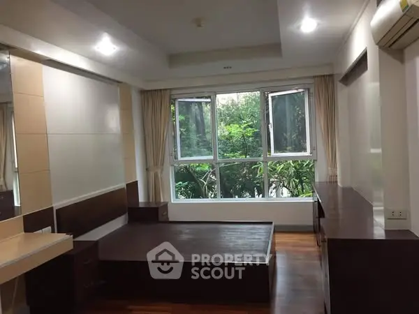 Spacious bedroom with large window and garden view, featuring modern wood furnishings.