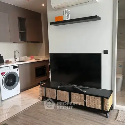 Modern apartment interior with sleek kitchen and cozy living area featuring a flat-screen TV and washing machine.