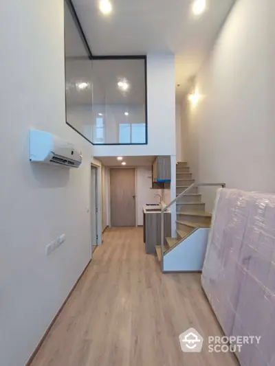 Modern loft-style apartment with mezzanine, sleek wooden flooring, and compact kitchen area.