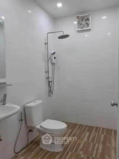 Modern bathroom with shower, toilet, and sink in sleek white design.