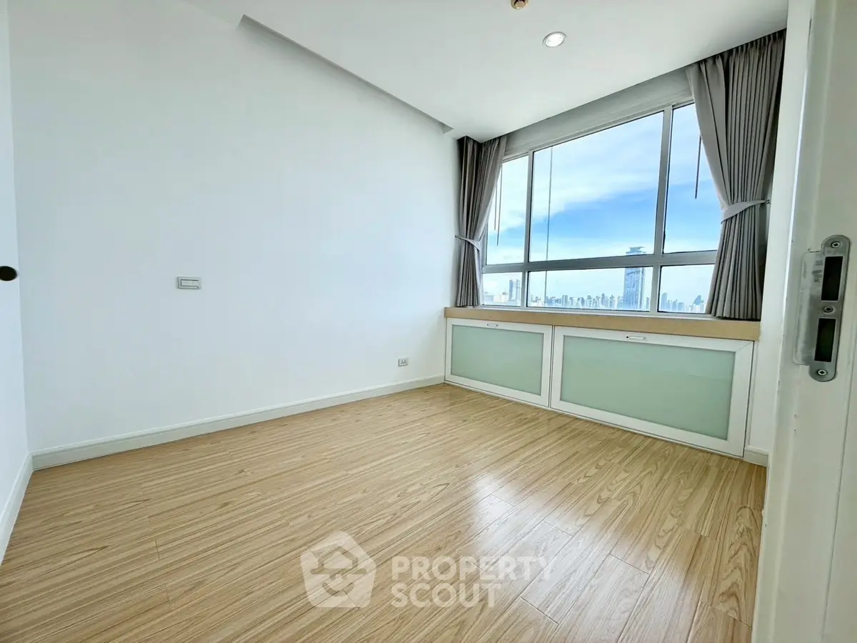 Bright bedroom with large window offering stunning city views and elegant wooden flooring.