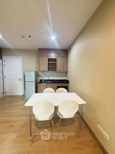 Modern kitchen with dining area featuring sleek wooden cabinets and a compact fridge.