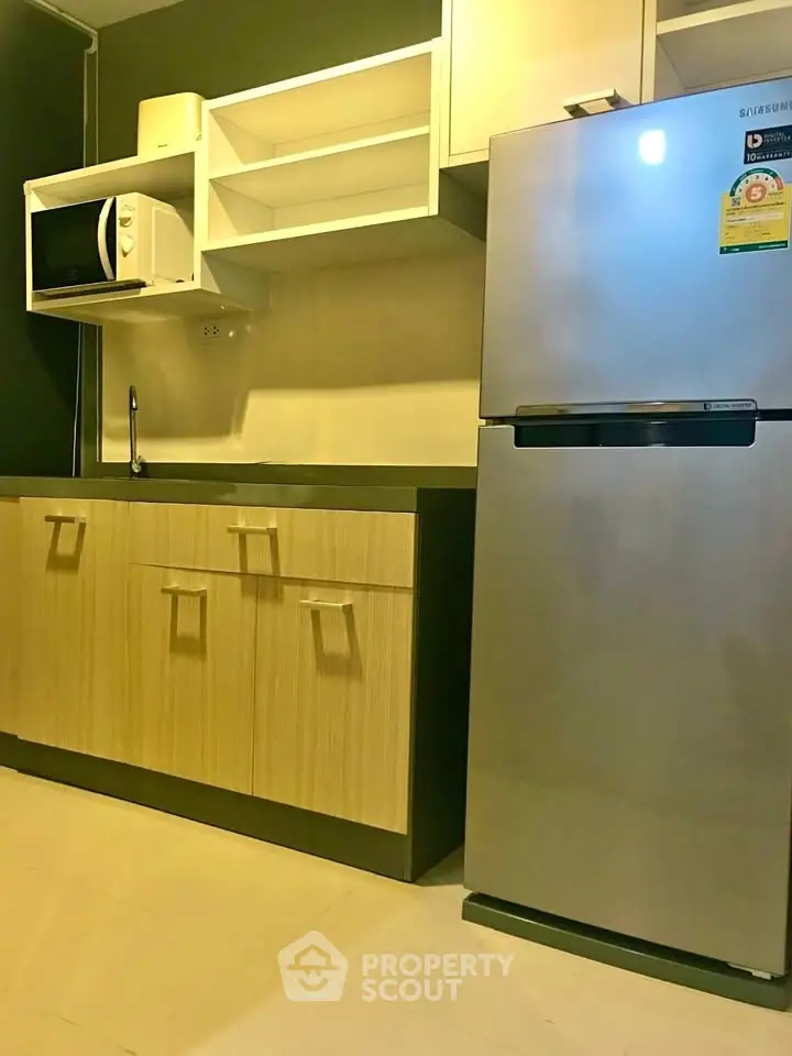 Modern kitchen with sleek cabinets, microwave, and stainless steel fridge in a stylish apartment.