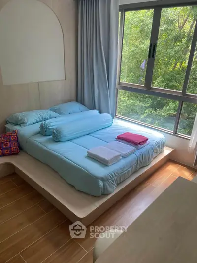 Cozy bedroom with large window and serene forest view, featuring a modern platform bed and wooden flooring.