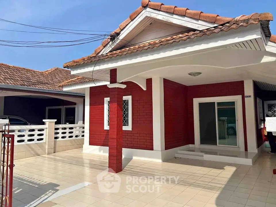Charming single-story house with red brick facade and tiled roof, featuring a spacious front patio.