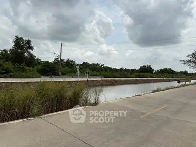 Scenic view of a rural road alongside a tranquil canal under a cloudy sky.