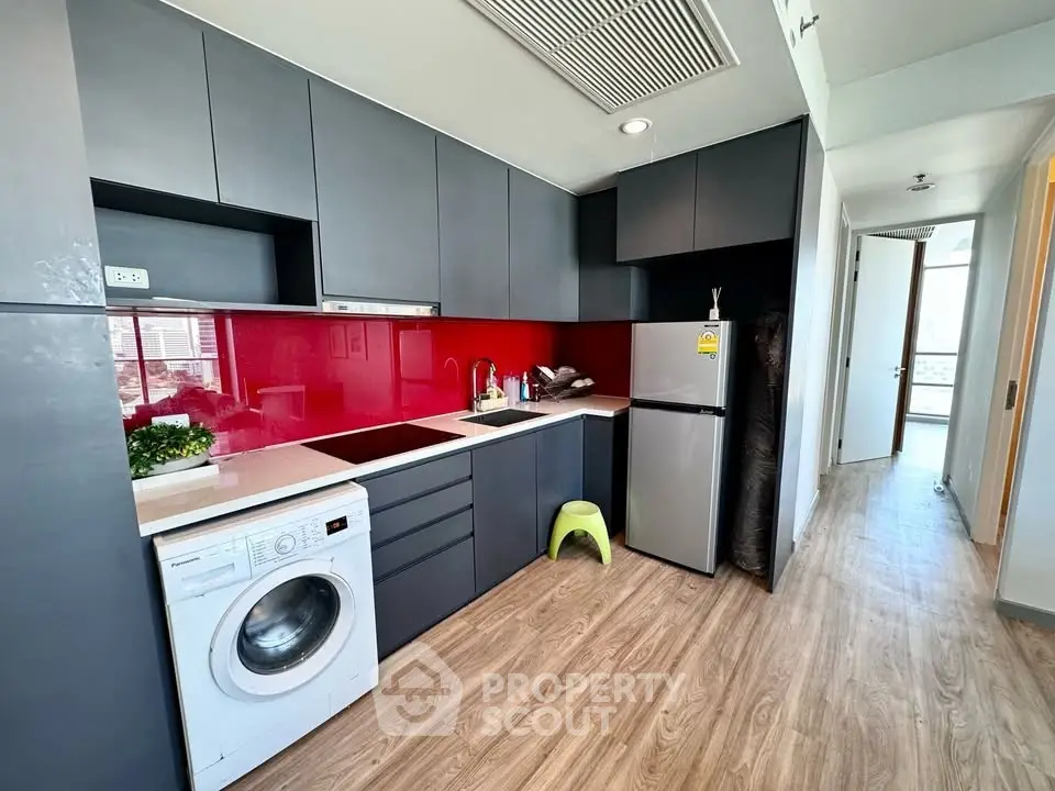 Modern kitchen with sleek cabinets, red backsplash, and in-unit washing machine.