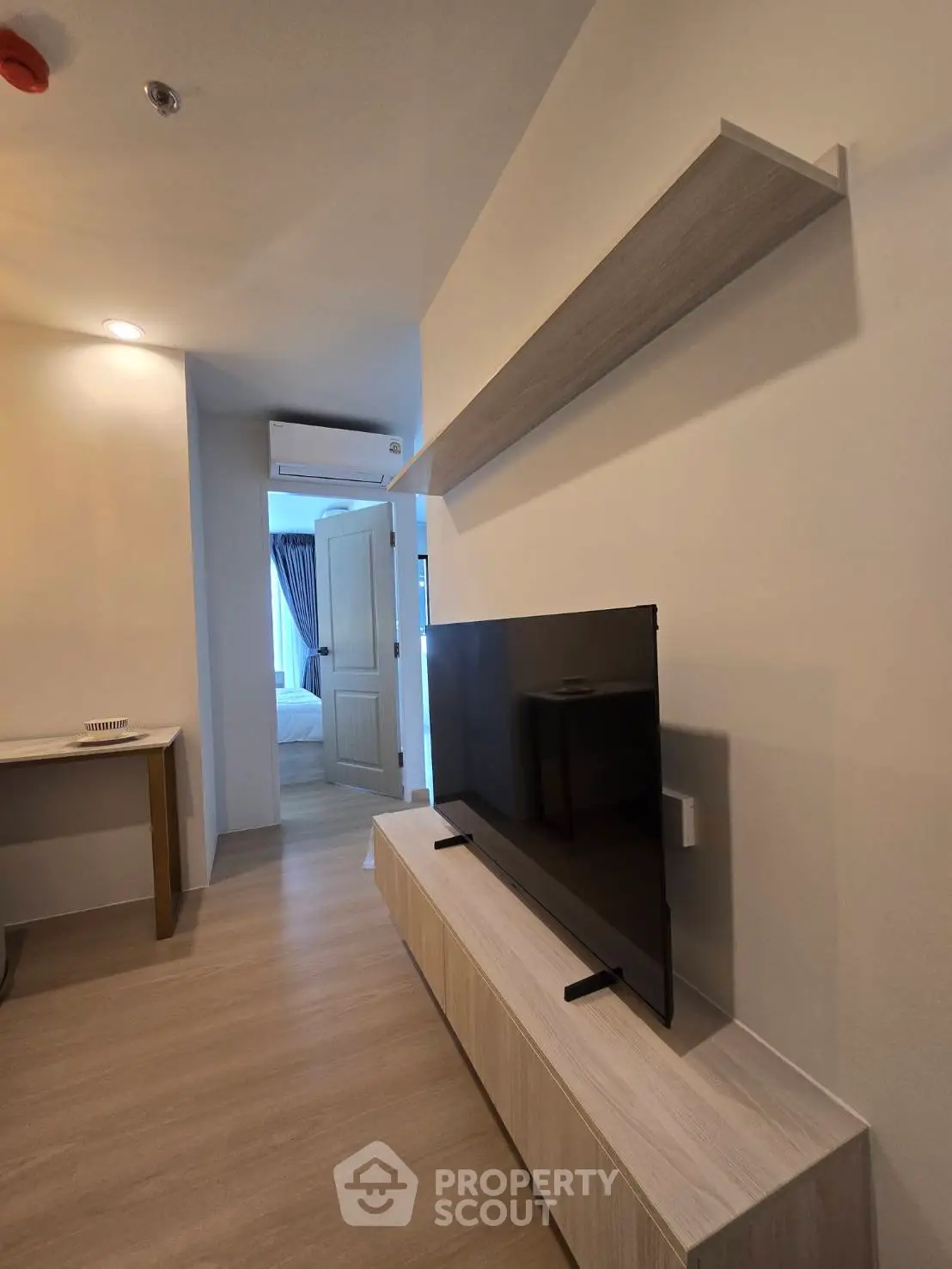 Modern living room with sleek TV stand and wall-mounted shelf, leading to a cozy bedroom.