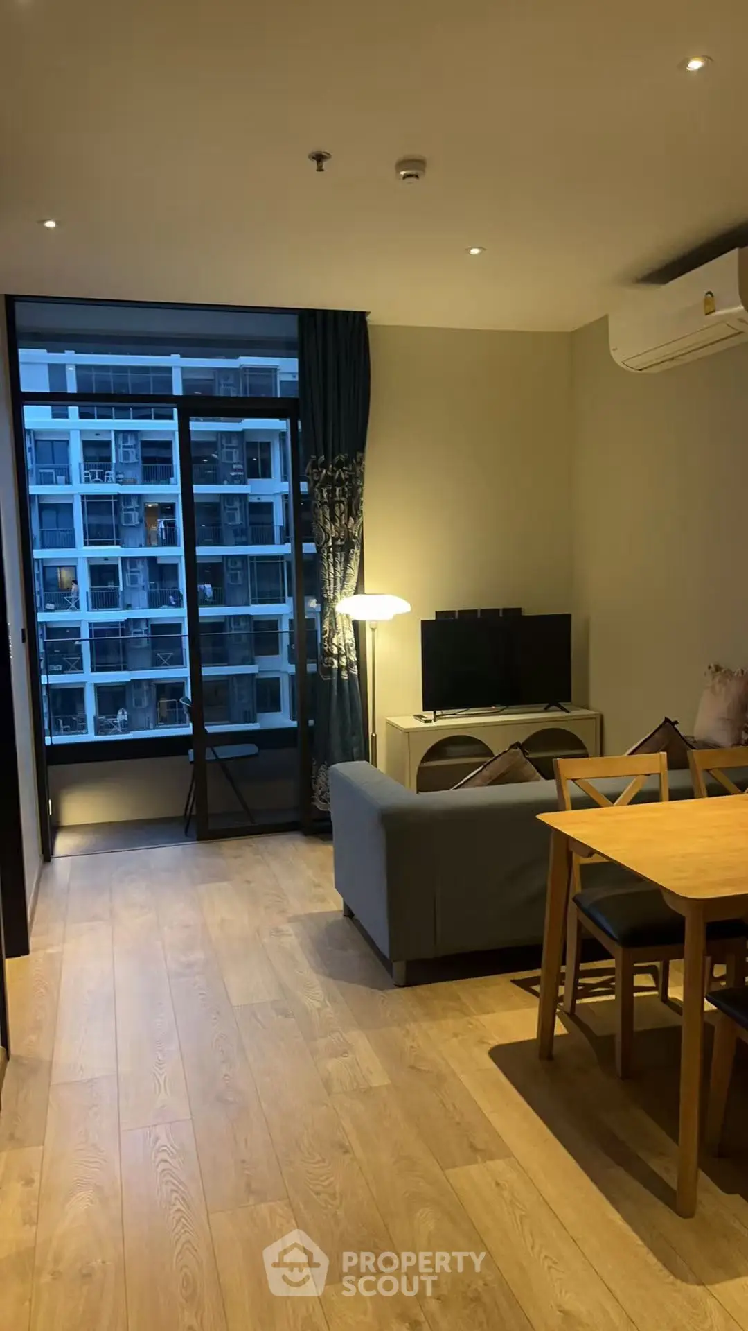 Modern living room with wooden flooring and balcony view in urban apartment.