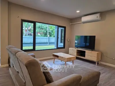 Modern living room with large window and stylish furniture, featuring a cozy sofa and sleek TV setup.