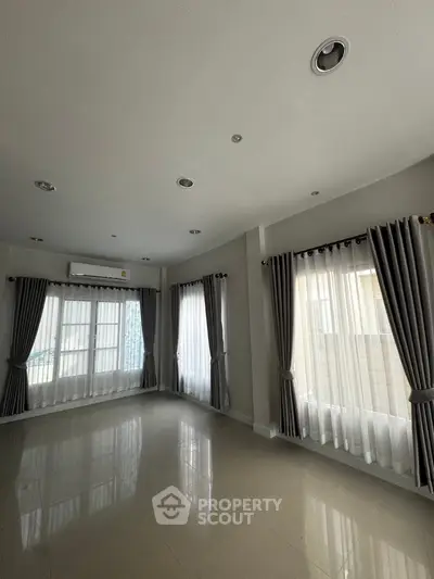 Spacious unfurnished living room with large windows and elegant curtains