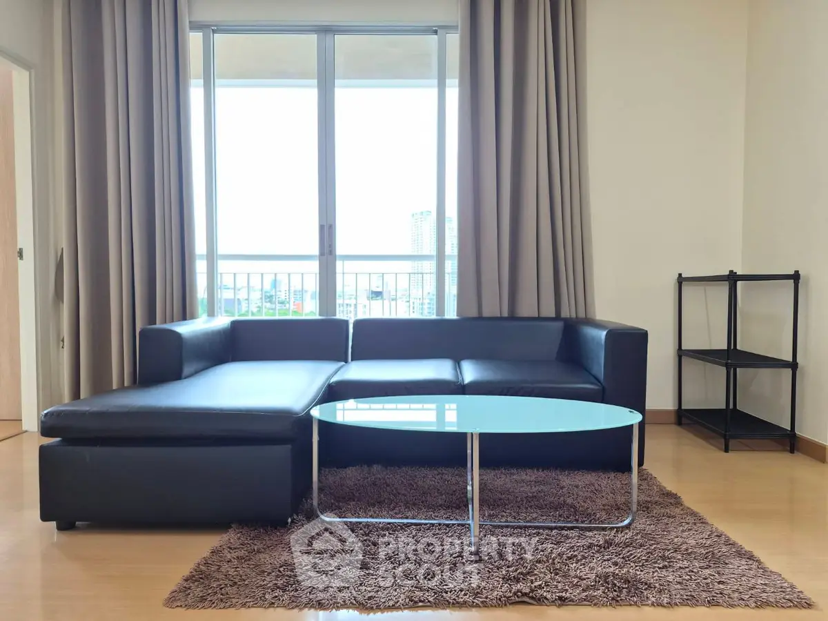 Modern living room with sleek black sofa and glass coffee table, featuring large windows and natural light.