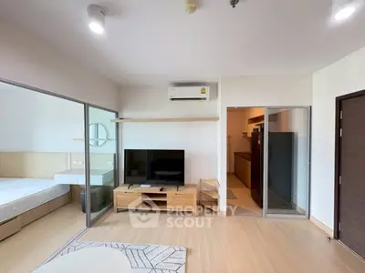 Modern living room with wooden flooring, TV unit, and sliding glass doors leading to bedroom and kitchen.