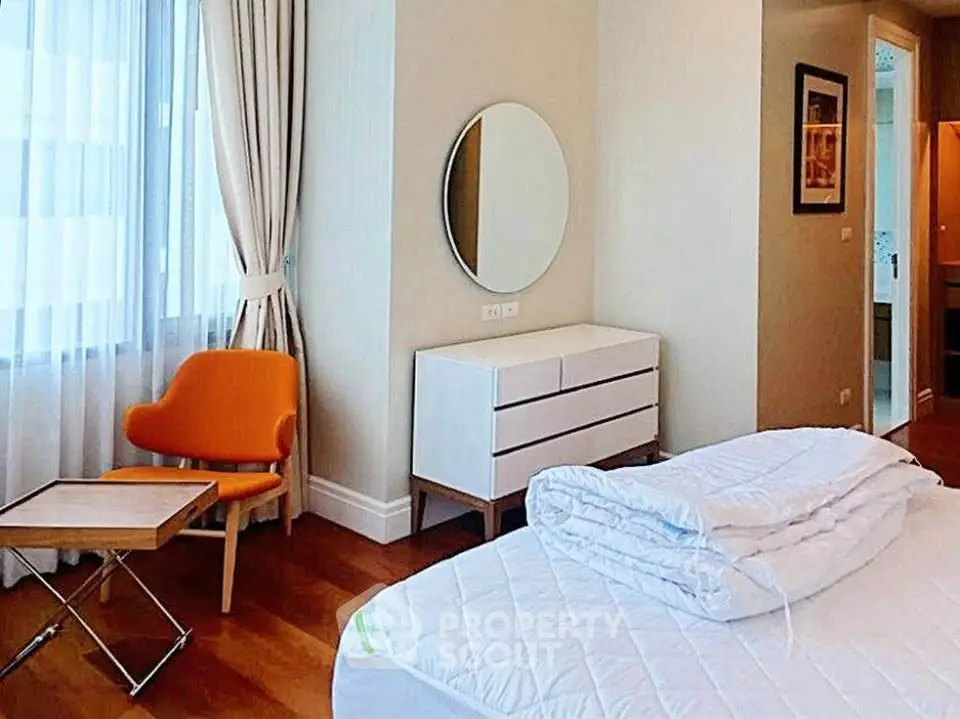 Modern bedroom with stylish furniture and natural light, featuring a cozy orange chair and elegant decor.