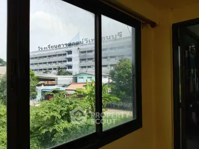 Spacious room with large window offering a scenic view of nearby buildings and lush greenery.