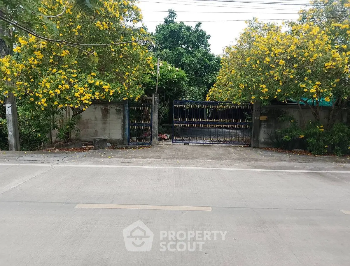 Charming gated entrance with lush greenery and vibrant yellow flowers, perfect for a serene residential property.