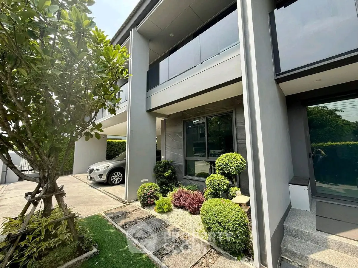 Modern two-story house with landscaped garden and carport, showcasing contemporary architecture and lush greenery.