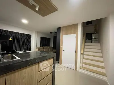 Modern open-plan living area with sleek kitchen and staircase in stylish apartment.