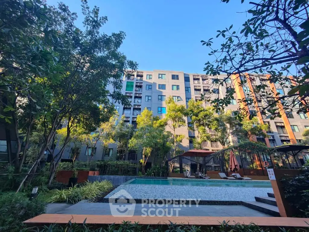 Modern apartment building with lush garden and inviting pool area under clear blue sky.