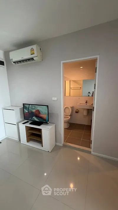 Modern living room with TV and air conditioning, adjacent to a bathroom in a sleek apartment.