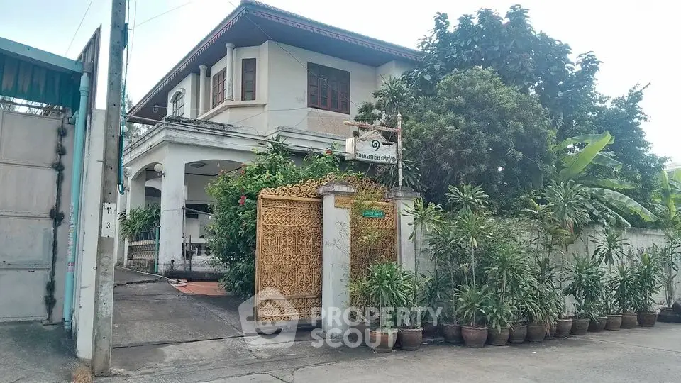 Charming two-story house with lush garden and ornate gate in serene neighborhood.