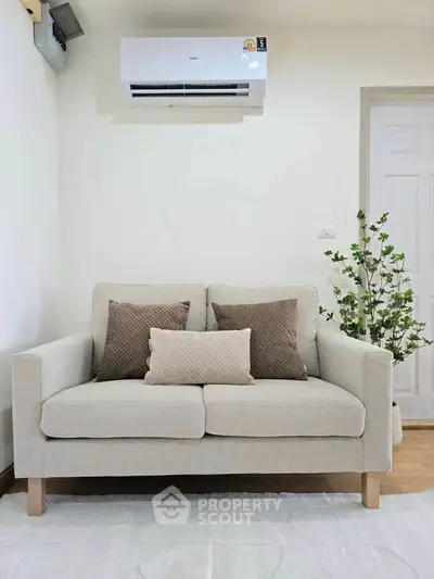 Cozy living room with modern beige sofa and air conditioning unit, perfect for relaxation.