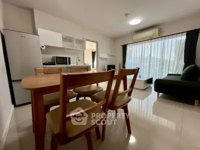 Modern open-plan living room with dining area and kitchen, featuring sleek furniture and ample natural light.