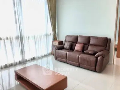 Spacious living room with leather sofa and large windows offering natural light.