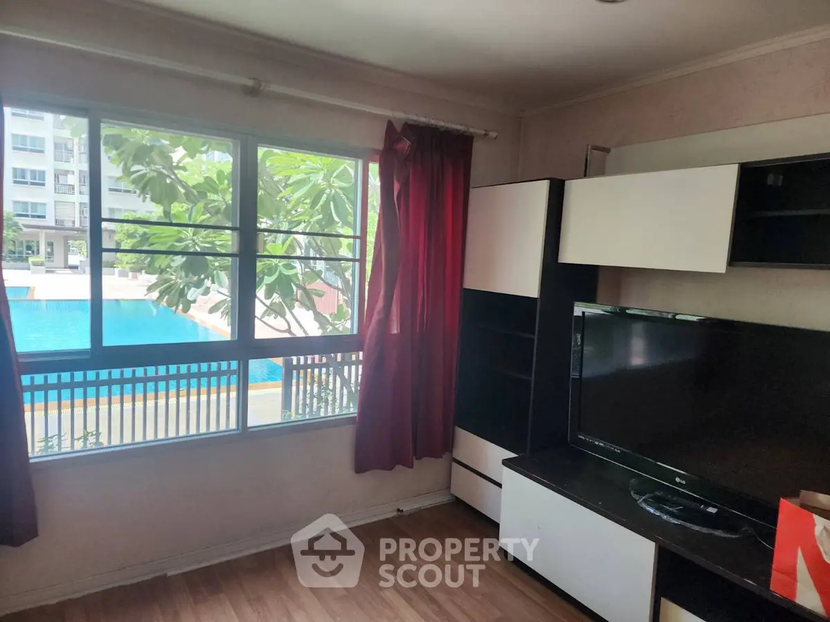 Cozy living room with pool view, featuring modern TV setup and large window for natural light.