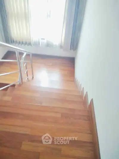 Elegant wooden staircase with sleek metal railing and natural light from window.
