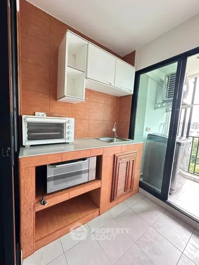 Modern kitchen with wooden cabinetry, microwave, and balcony view in a stylish apartment.