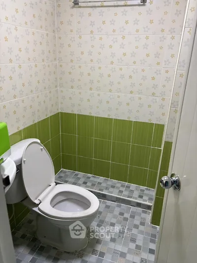 Compact bathroom with green and white tile design, featuring a standard toilet and modern aesthetic.