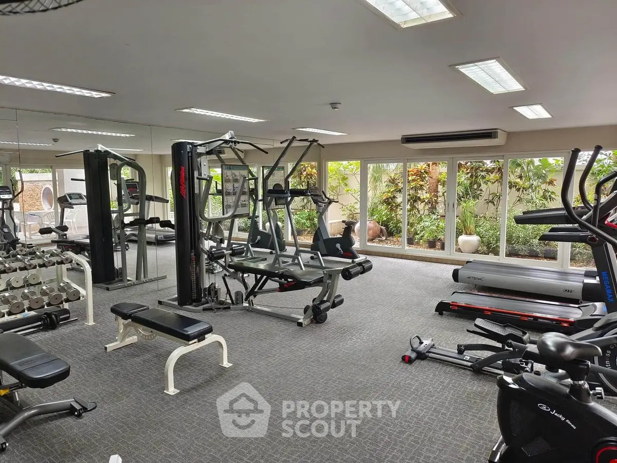 Spacious gym with modern equipment and garden view in luxury residential complex.