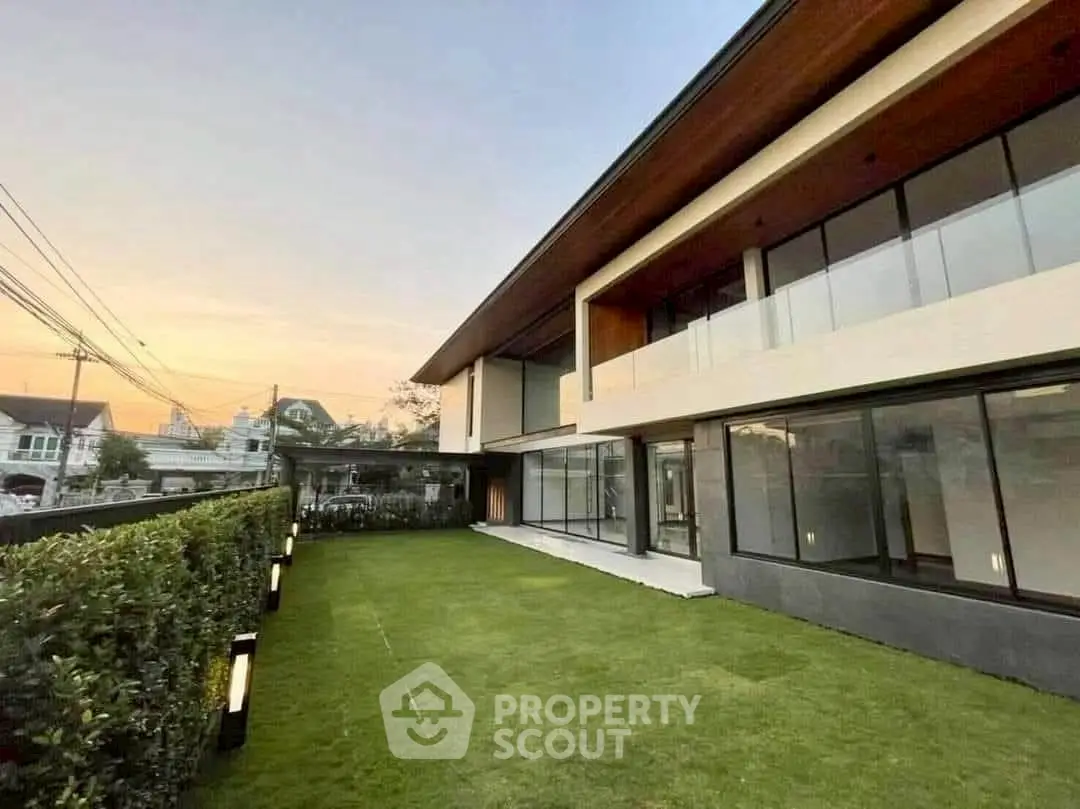 Modern two-story house with large windows and spacious lawn at sunset.