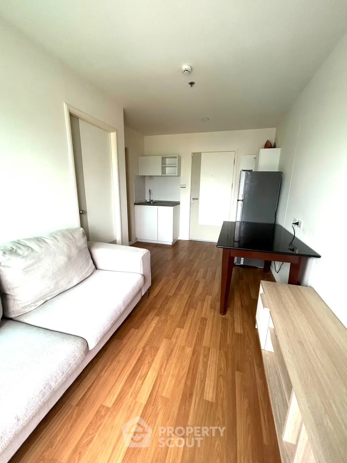 Modern living room with wooden flooring and compact kitchen area in a cozy apartment.