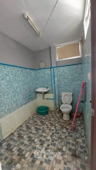 Spacious bathroom with tiled walls and floor, featuring a toilet and sink.