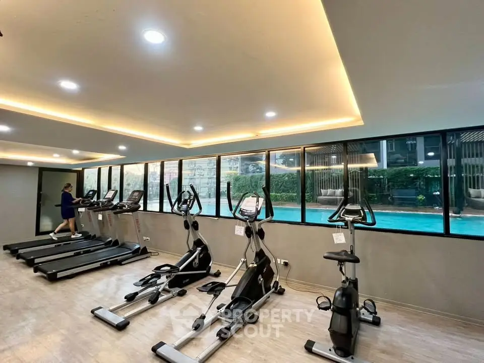 Modern gym with pool view, featuring state-of-the-art exercise equipment and stylish lighting.