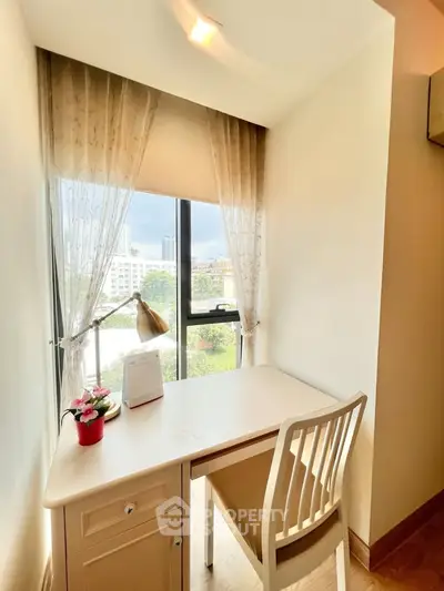 Cozy study nook with a view, featuring a desk and chair by a window with sheer curtains.