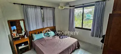 Cozy bedroom with large windows and natural light, featuring a wooden bed and dresser.