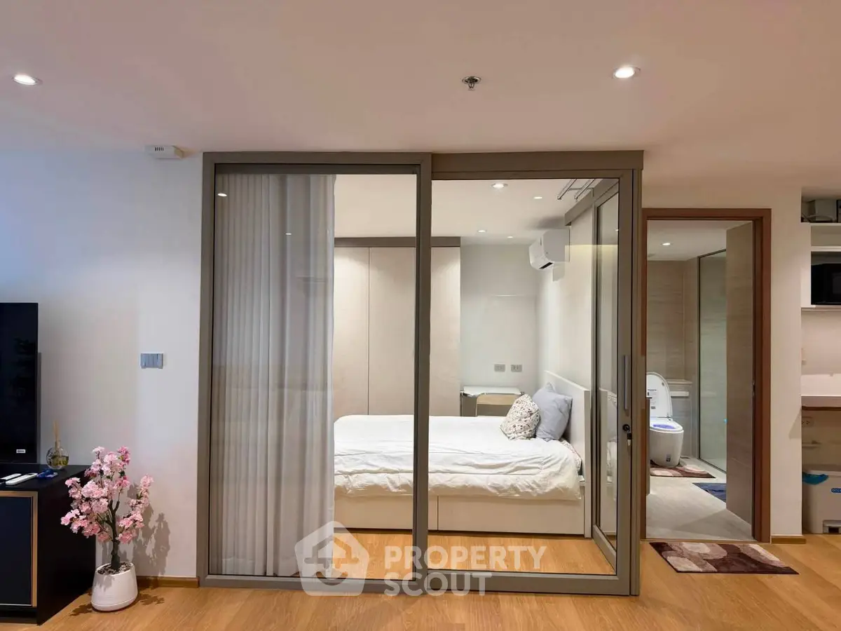 Modern bedroom with sliding glass doors and ensuite bathroom in a stylish apartment.