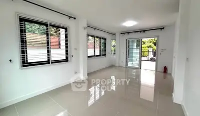 Spacious living room with glossy tiles and large windows opening to a lush garden view.