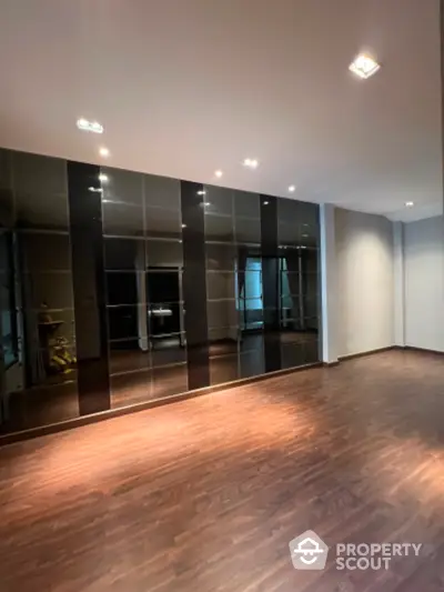 Spacious and modern living room with glossy hardwood floors and a full wall of mirrored closets reflecting ambient lighting.