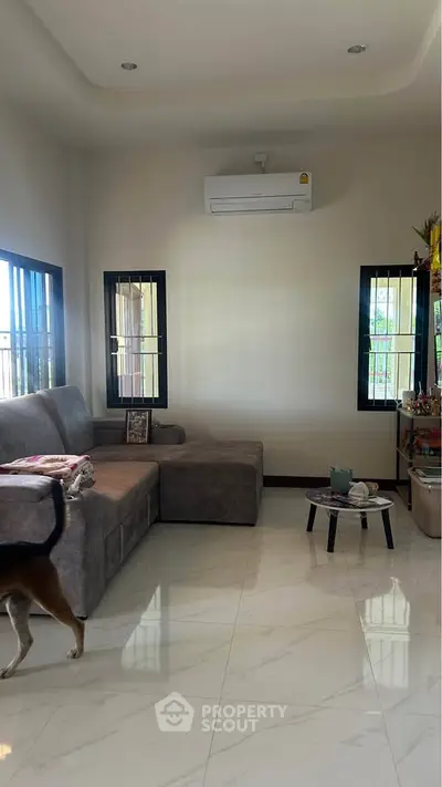 Spacious living room with modern sofa and air conditioning, featuring elegant tiled flooring and natural light.