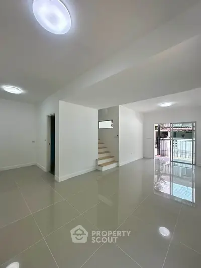 Spacious modern living room with glossy tiled floors and staircase, perfect for contemporary living.