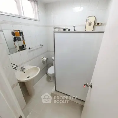 Compact bathroom with modern fixtures and tiled walls, featuring a shower and small window.