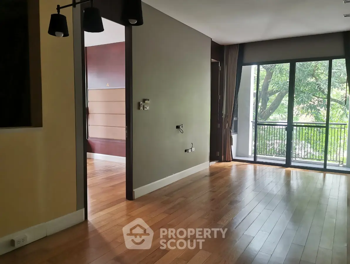 Spacious living room with wooden flooring and large windows overlooking greenery.