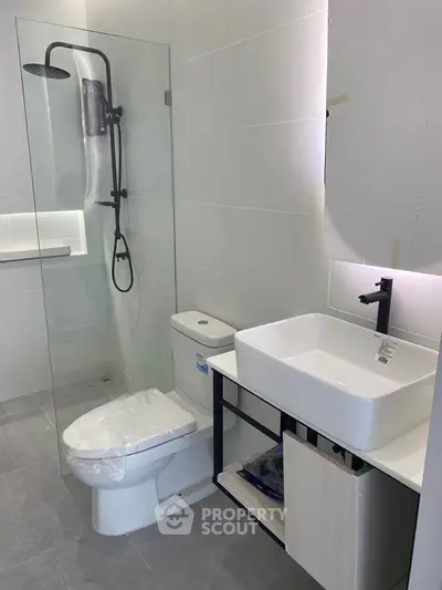 Modern bathroom with glass shower, sleek sink, and toilet in contemporary apartment.